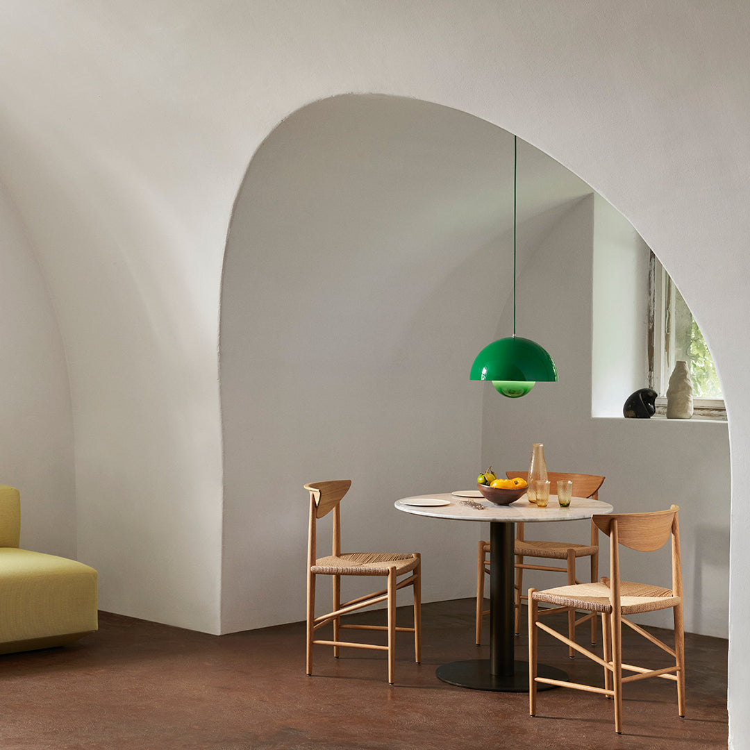 Green pendant light over a round table, wooden chairs, and earthy-toned floor in an elegant, arched interior space.
