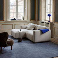Cream sectional sofa with a blue throw, set against a muted gray rug and elegant patterned walls.