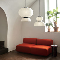 Modern orange couch with white pendant lights and green plants against a soft neutral backdrop.
