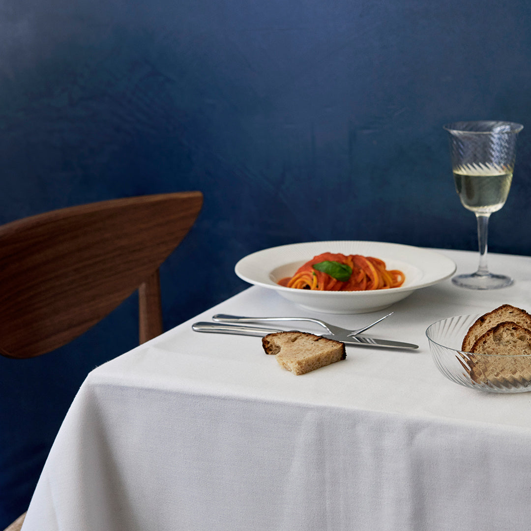 White tablecloth with textured surface, blue wall background, and subtle earth tones from food and glassware.