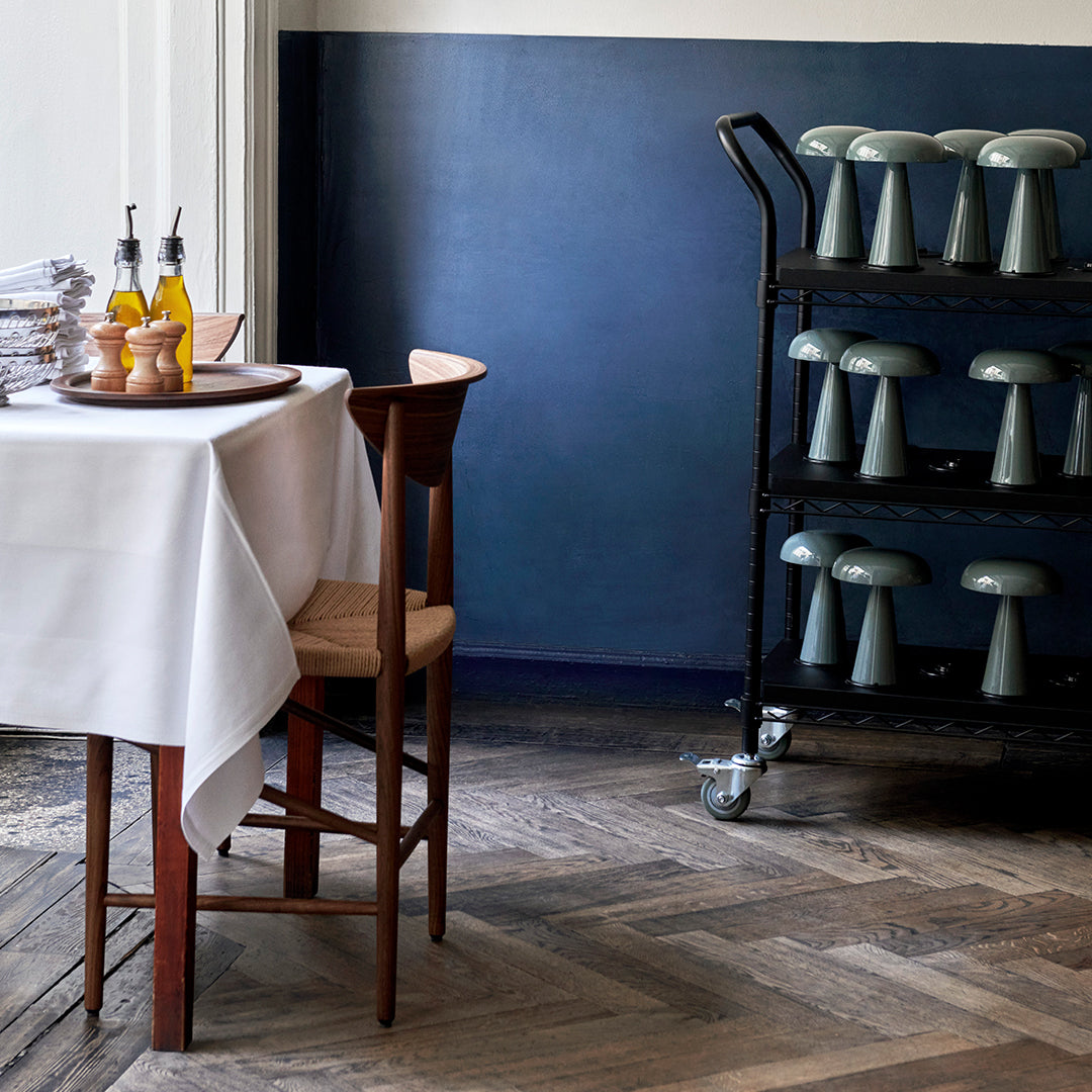 "Elegant white tablecloth on wooden table, deep blue wall, and gray mushroom-shaped decor on a black cart."