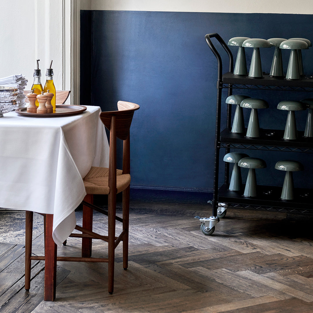 "Elegant dining setup with a white tablecloth, blue wall, and teal mushroom decor against a patterned wooden floor."