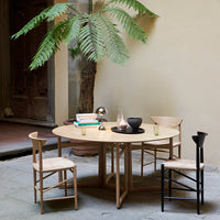 Natural wood table with round shape, paired with light and dark chairs, surrounded by greenery and neutral tones.