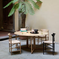 Light wood round dining table with minimalist black chairs, complemented by greenery, creating a natural, inviting ambiance.