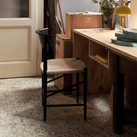 Natural wood and black accent dining chair with woven seat, paired with a neutral-toned floor and light wooden table.