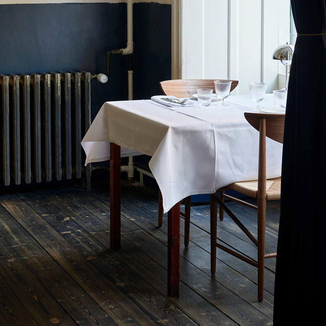 White tablecloth on wooden table, contrasting with dark blue wall and rustic wooden floor for a minimalist dining look.