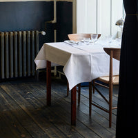 White tablecloth on wooden table, contrasting with dark blue wall and rustic wooden floor for a minimalist dining look.