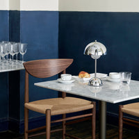 Wooden and chrome table lamp on a marble table, with a navy blue wall backdrop and neutral-toned furniture.