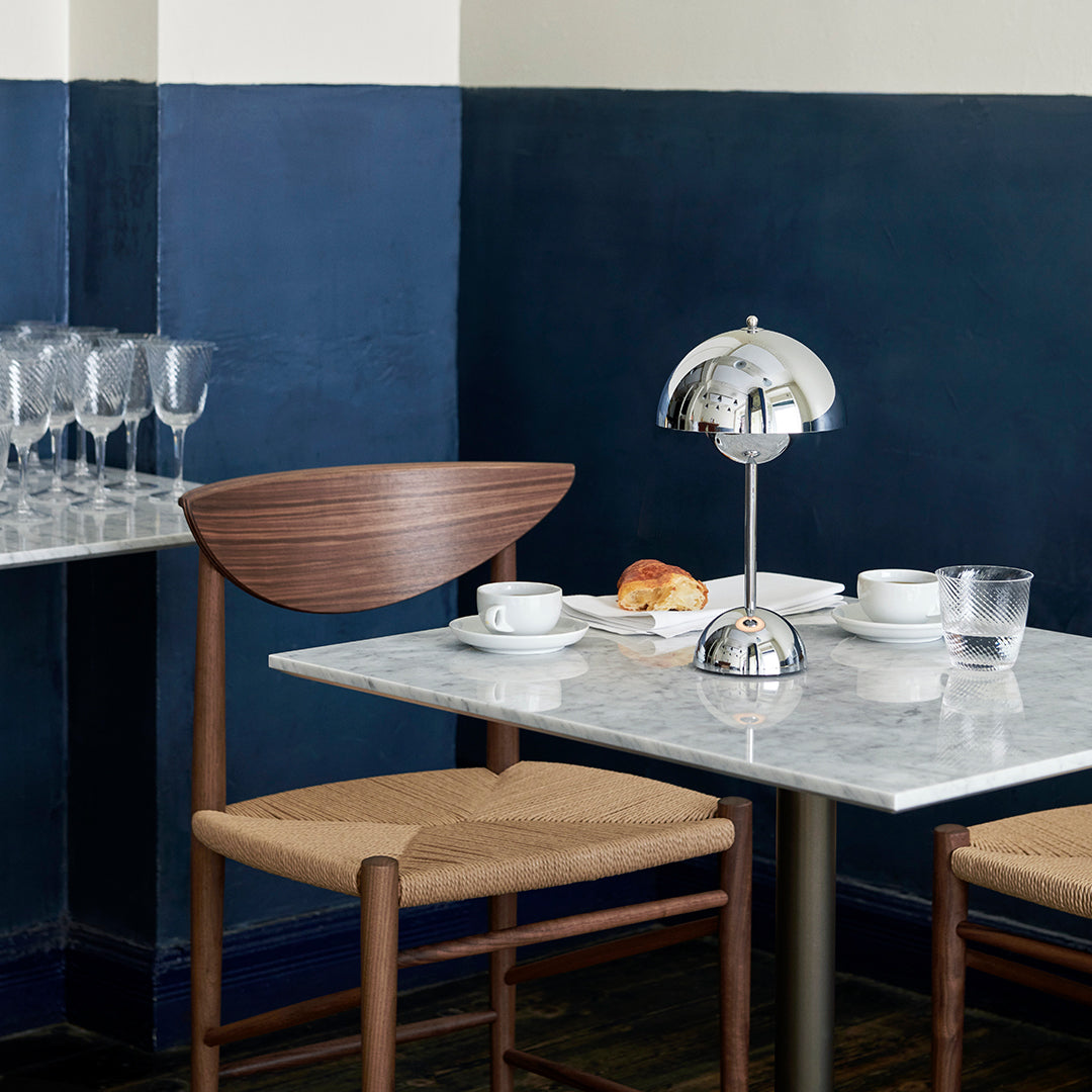 Wooden and chrome table lamp on a marble table, with a navy blue wall backdrop and neutral-toned furniture.