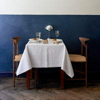 "Elegant white tablecloth on a wooden table against a deep blue wall, featuring subtle textures and natural wood tones."