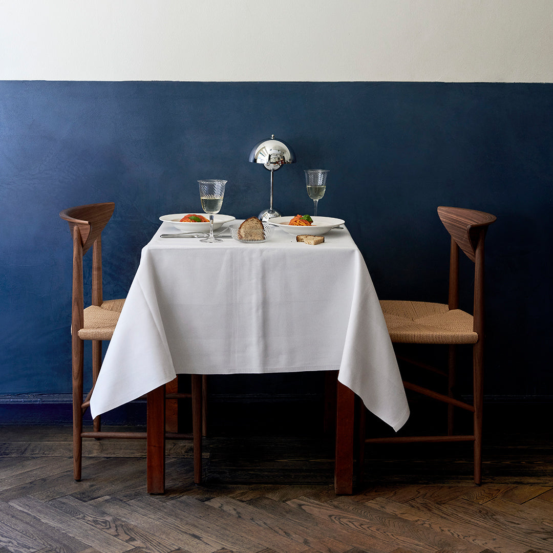 "Elegant white tablecloth on a wooden table against a deep blue wall, featuring subtle textures and natural wood tones."