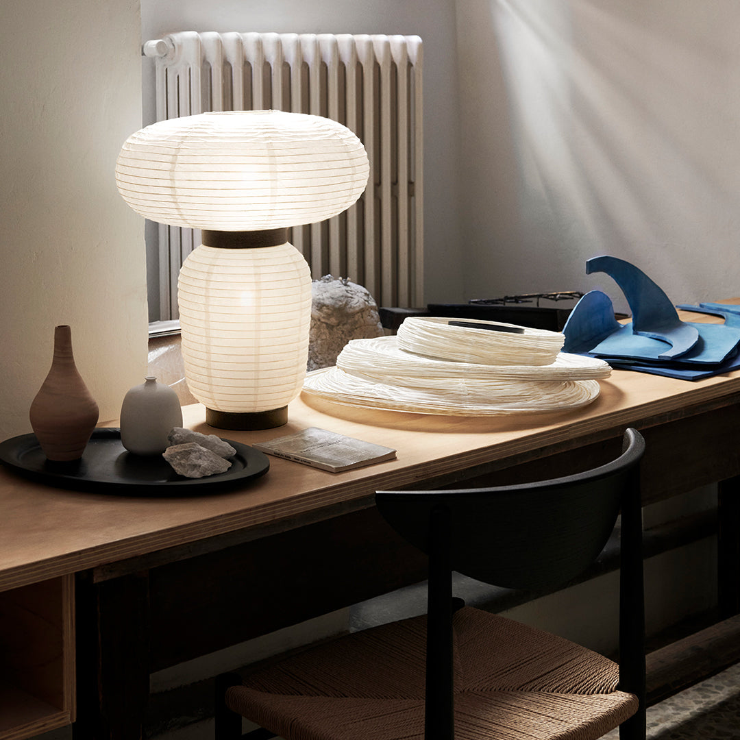 "White lamp with pleated shade, neutral decor elements, and blue accent pieces on a wooden table."
