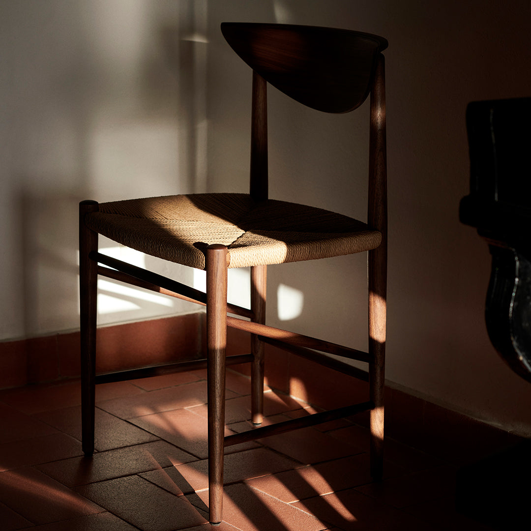 Wooden chair with a curved backrest, featuring natural tones and a woven seat, highlighted by soft light and shadows.