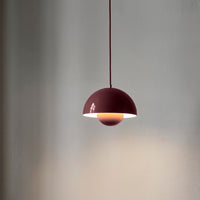 Burgundy pendant lamp with a sleek half-dome design and warm, glowing interior light, set against a minimalist background.