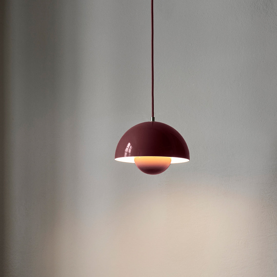 Burgundy pendant lamp with a sleek half-dome design and warm, glowing interior light, set against a minimalist background.