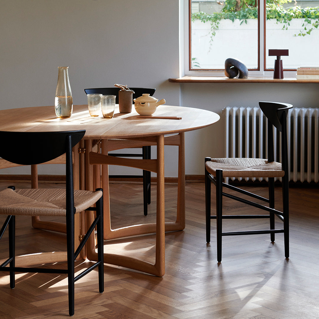 Light wood table with curved edges and black chairs featuring woven seats, set against warm-toned wood flooring.