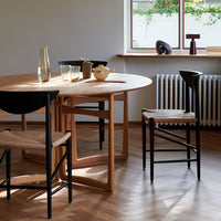 Light wood table with curved edges and black chairs featuring woven seats, set against warm-toned wood flooring.