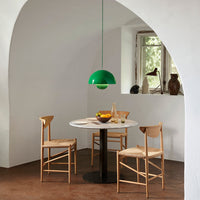 Green pendant light hanging over a round white table, surrounded by wooden chairs in a minimalist, neutral-toned setting.