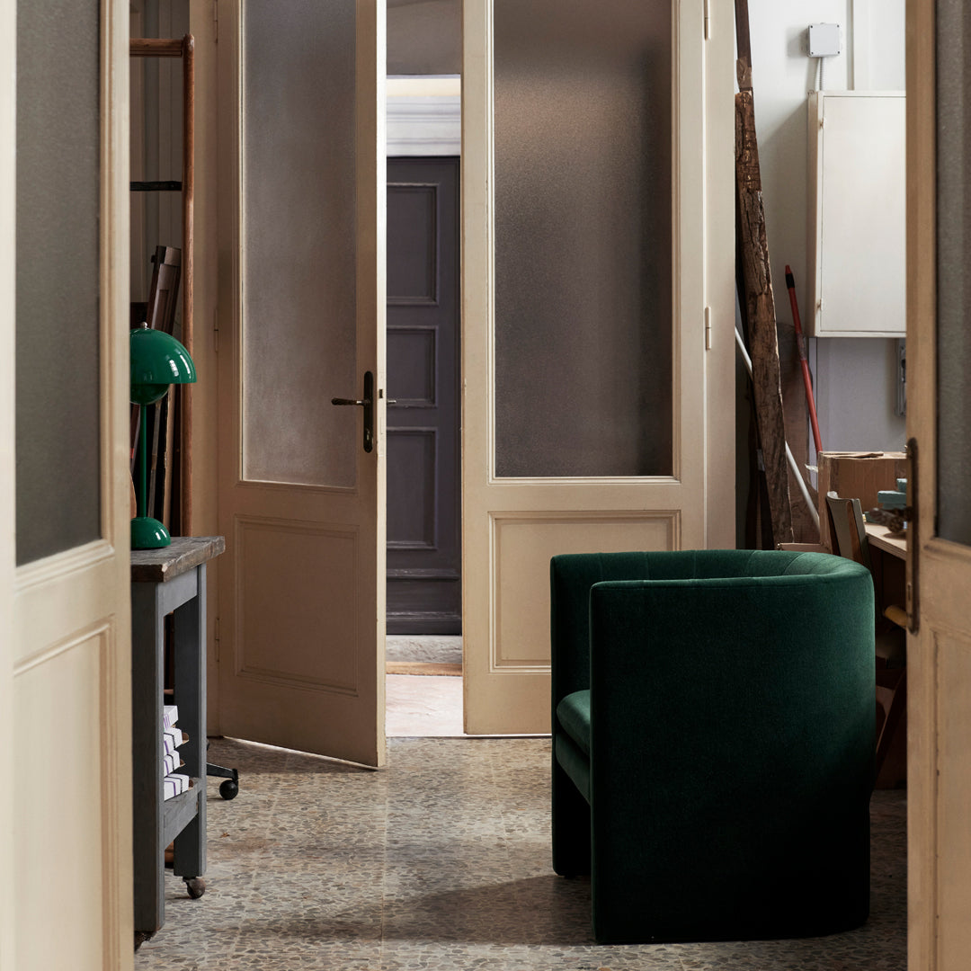 "Green velvet armchair in elegant hallway with muted tones and textured flooring."