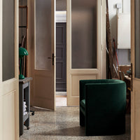 "Green velvet armchair in elegant hallway with muted tones and textured flooring."