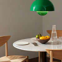 Green hanging lamp above a round marble table, wooden chairs, and a bowl of colorful fruits, creating a modern, vibrant setting.