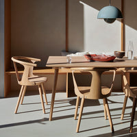 Light wood dining table with natural grain and minimalistic design, complemented by a soft blue pendant light.