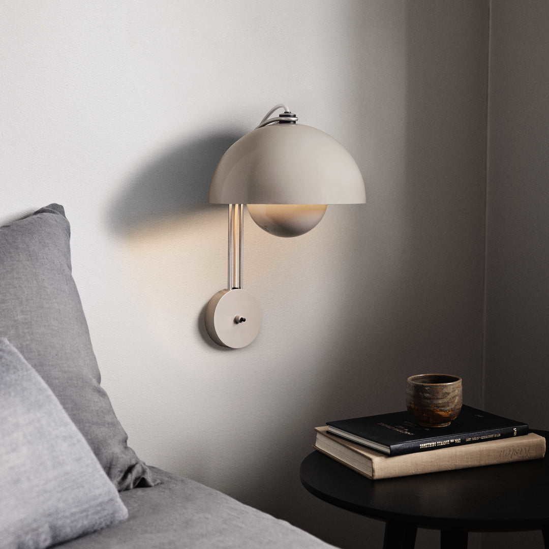 Modern beige wall lamp with a rounded shade, paired with a gray backdrop and black table décor.