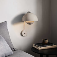 Modern beige wall lamp with a rounded shade, paired with a gray backdrop and black table décor.
