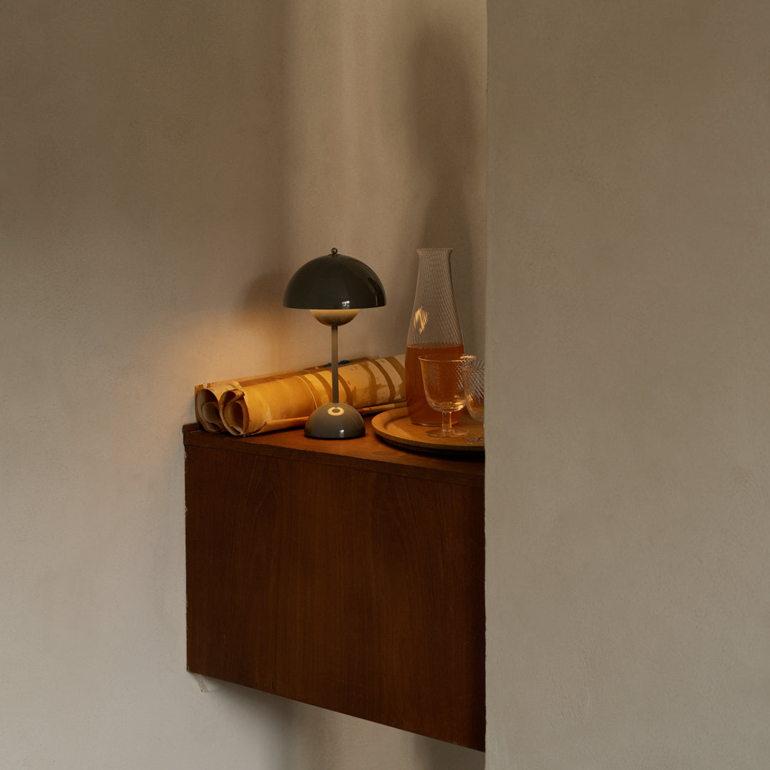 Wooden shelf with warm tones, paired with a green lamp and amber glass, accented by rolled paper and a circular tray.