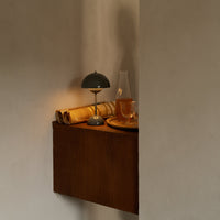 Wooden shelf with warm tones, paired with a green lamp and amber glass, accented by rolled paper and a circular tray.