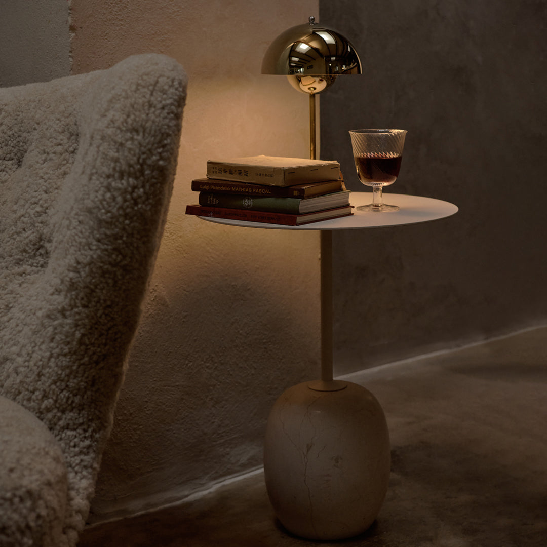 Modern white side table with smooth surface and organic stone base, paired with warm gold lamp and neutral-toned decor.