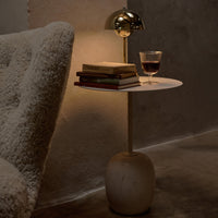 Modern white side table with smooth surface and organic stone base, paired with warm gold lamp and neutral-toned decor.
