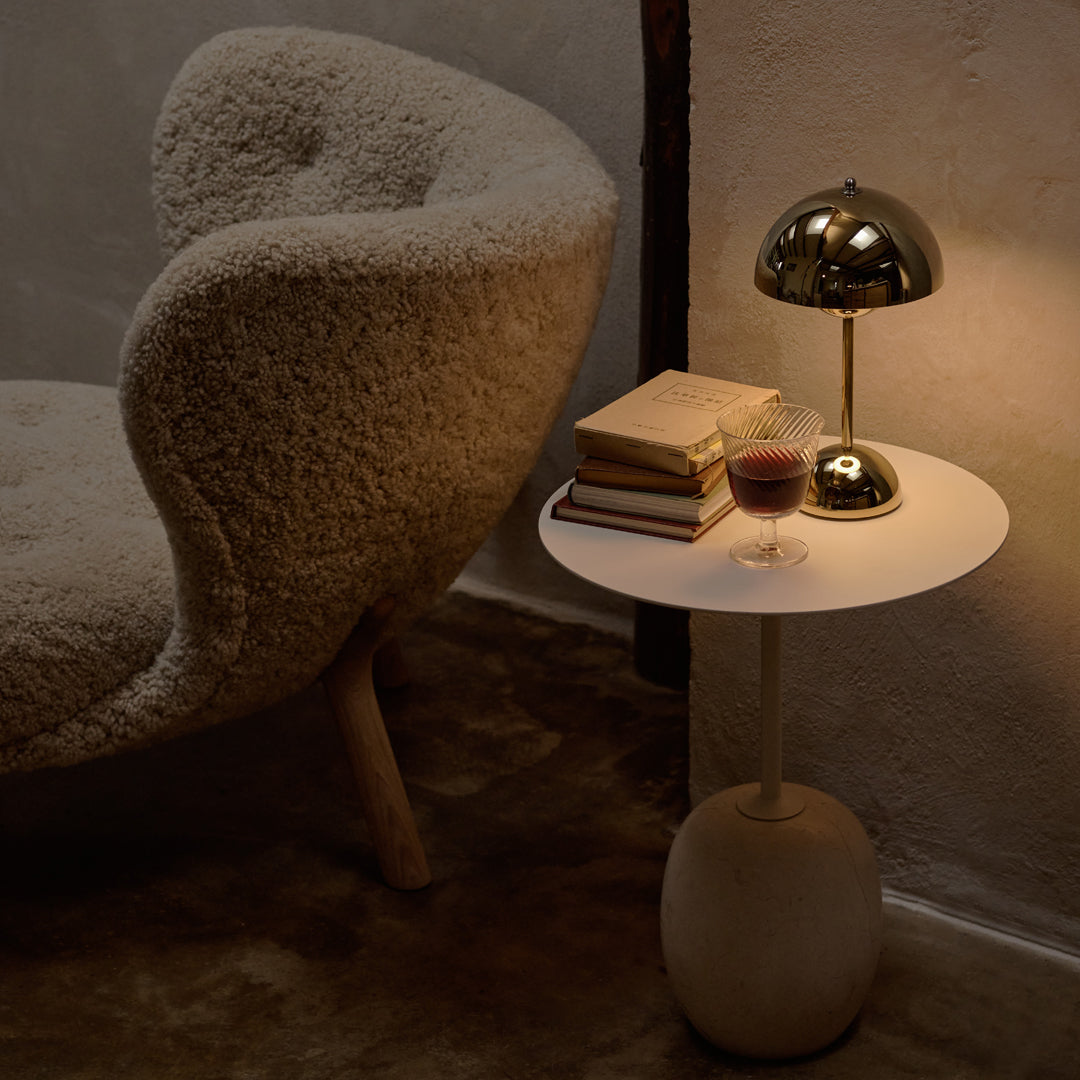 Cozy cream chair with fluffy texture beside a sleek white table, featuring gold accents and warm ambient lighting.