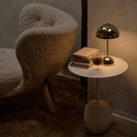 Cozy cream chair with fluffy texture beside a sleek white table, featuring gold accents and warm ambient lighting.