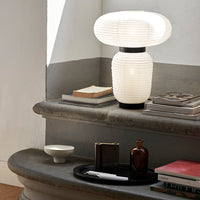 White lantern-style lamp with pleated texture, contrasting black base and surrounding neutral decor elements.