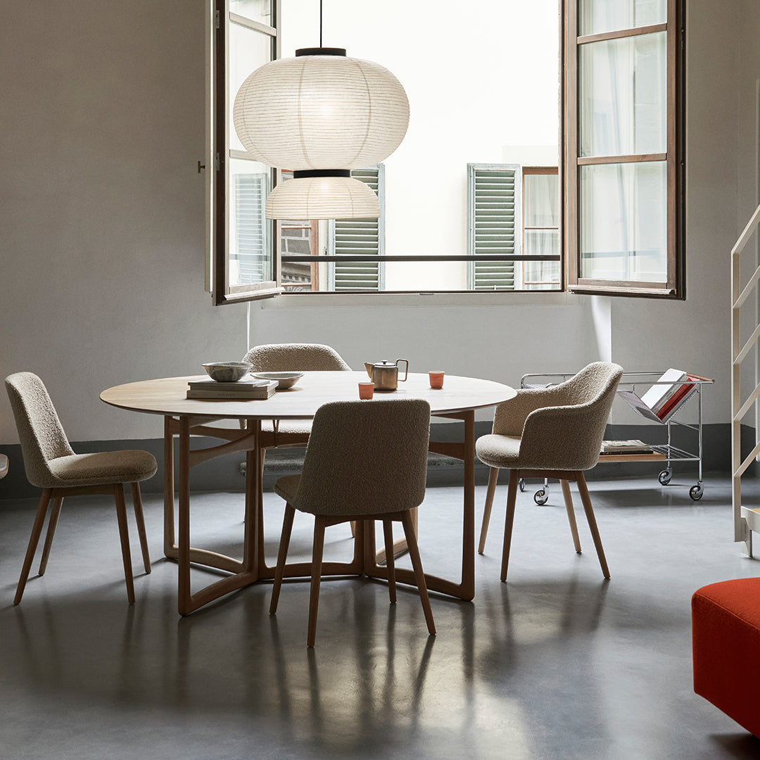 Modern round dining table with beige chairs, warm wood accents, and a neutral color palette in a bright, airy room.