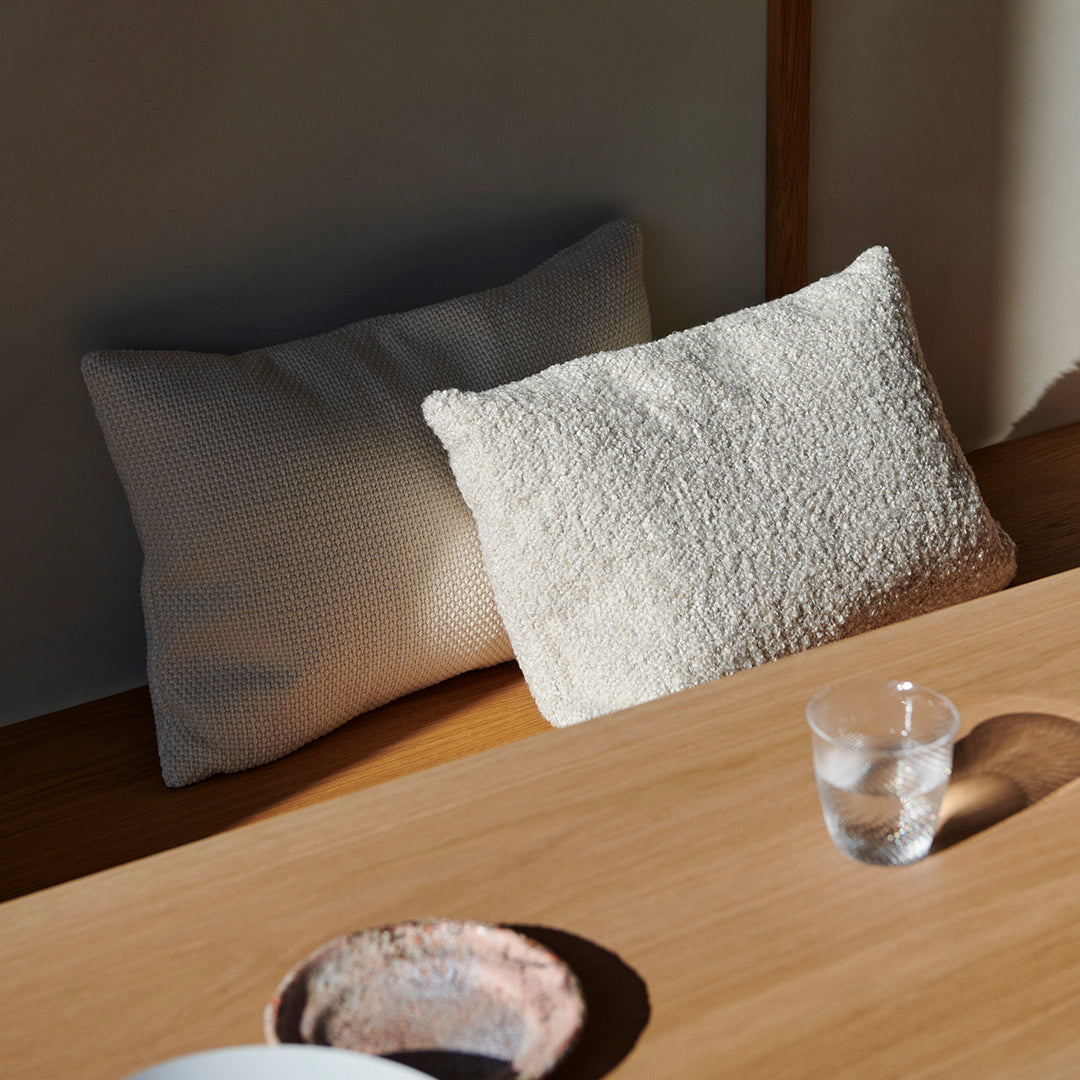 Two decorative pillows in soft cream textures, featuring a cozy, plush look and subtle ribbed pattern, arranged on a wooden table.