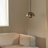 Elegant silver pendant light hanging above a soft beige couch in a modern interior setting.