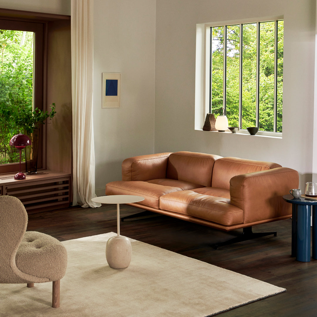 Tan leather sofa with minimalist design, complemented by a beige rug and light-colored curtains in a bright room.