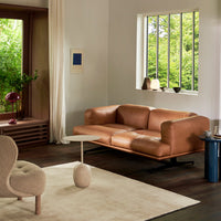 "Tan leather sofa and beige accent chair on a light rug, set in a bright room with greenery and natural accents."