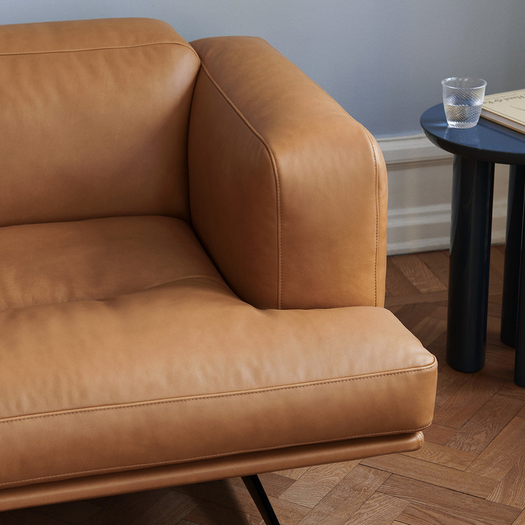 Tan leather sofa with smooth texture, complemented by a minimalist black side table and warm wood flooring.