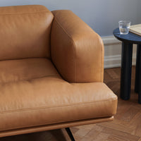 Tan leather sofa with smooth texture, complemented by a minimalist black side table and warm wood flooring.