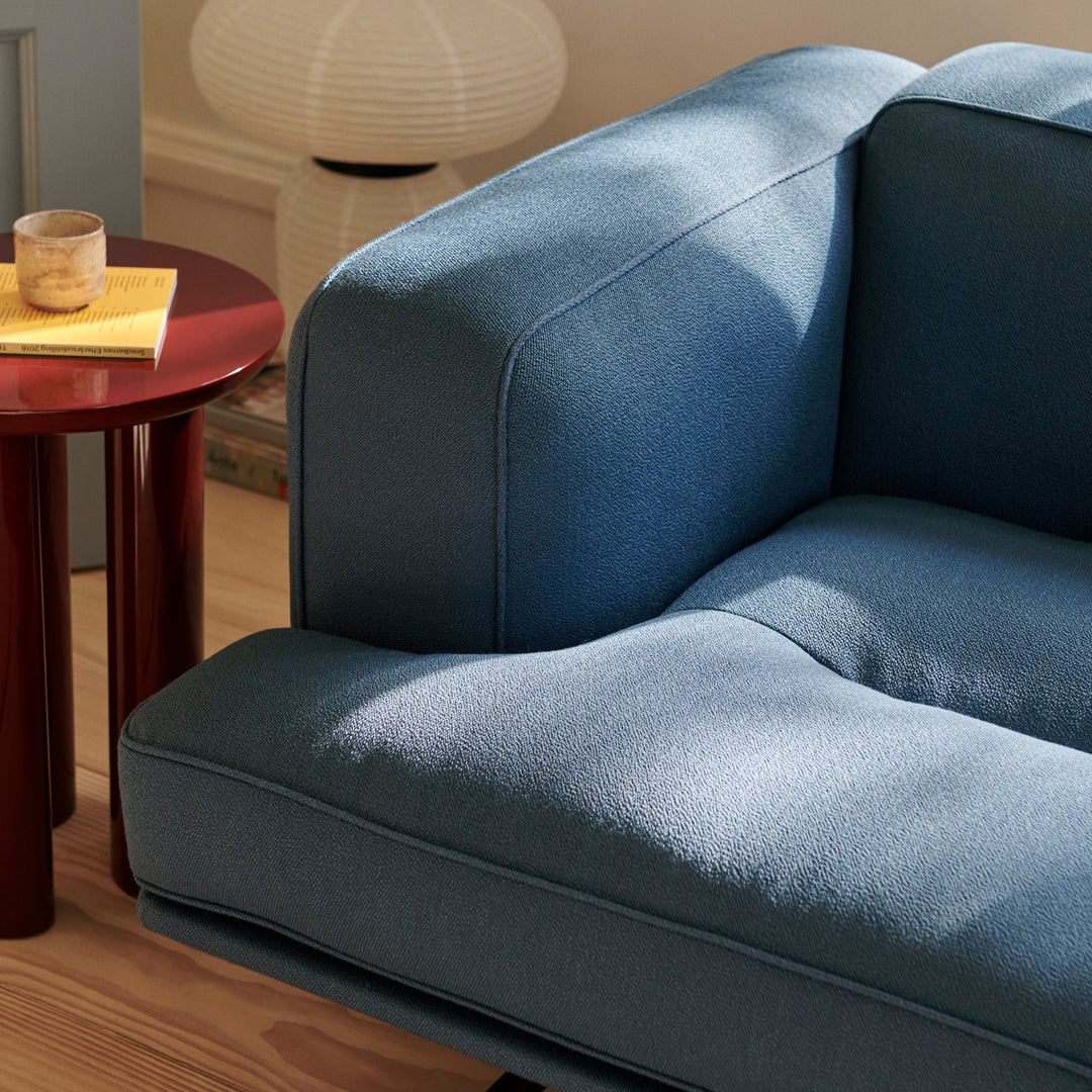 Blue textured sofa with a modern design, paired with a round red accent table. Elegant and contemporary colors.
