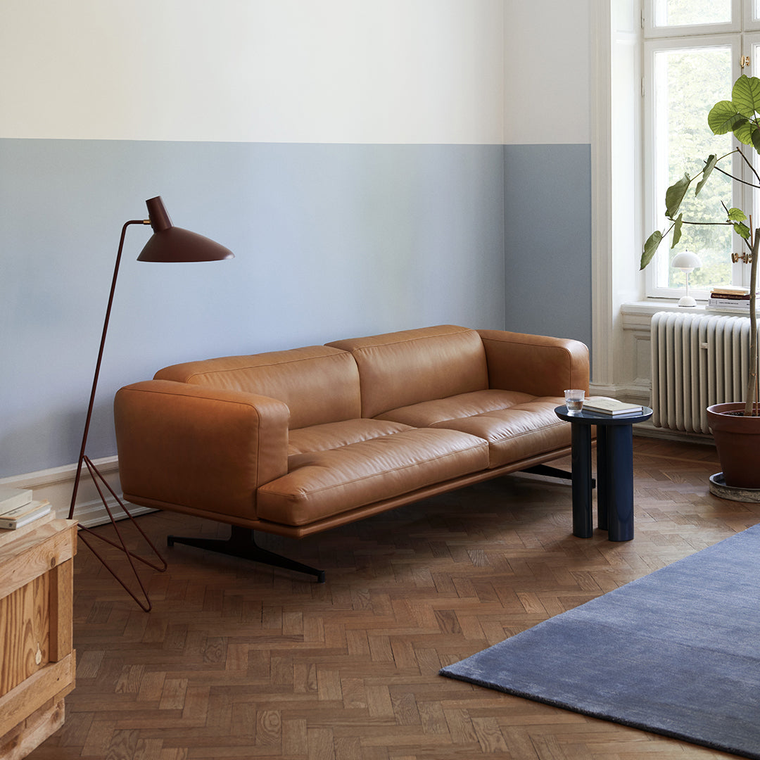 Brown leather sofa with sleek lines, set against a light blue and white wall and a patterned blue rug.