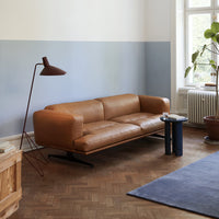 Brown leather sofa with sleek lines, set against a light blue and white wall and a patterned blue rug.