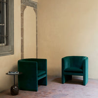 Green velvet armchairs with a sleek, modern design against a neutral beige wall, highlighting elegant textures.