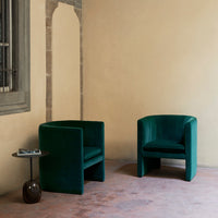Velvet green armchairs with sleek, modern design against a soft beige wall, creating a stylish contrast.