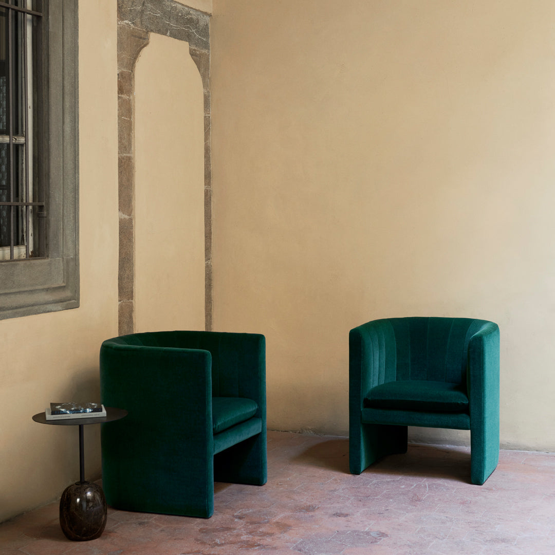 Green velvet armchairs with a sleek, modern design against a neutral beige wall, highlighting elegant textures.