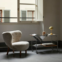 Soft beige textured armchair with wooden legs beside a sleek metallic table featuring neutral-toned decor accents.