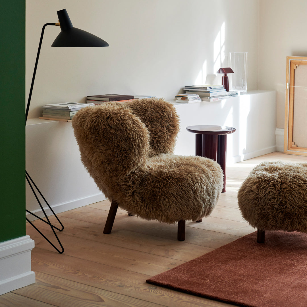 Fuzzy beige armchair and ottoman on a warm wood floor, complemented by a green wall and a deep red rug.